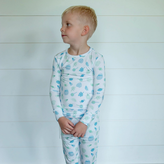A young child wearing a white long-sleeve pajama set with a light blue cloud pattern, standing against a white paneled wall.